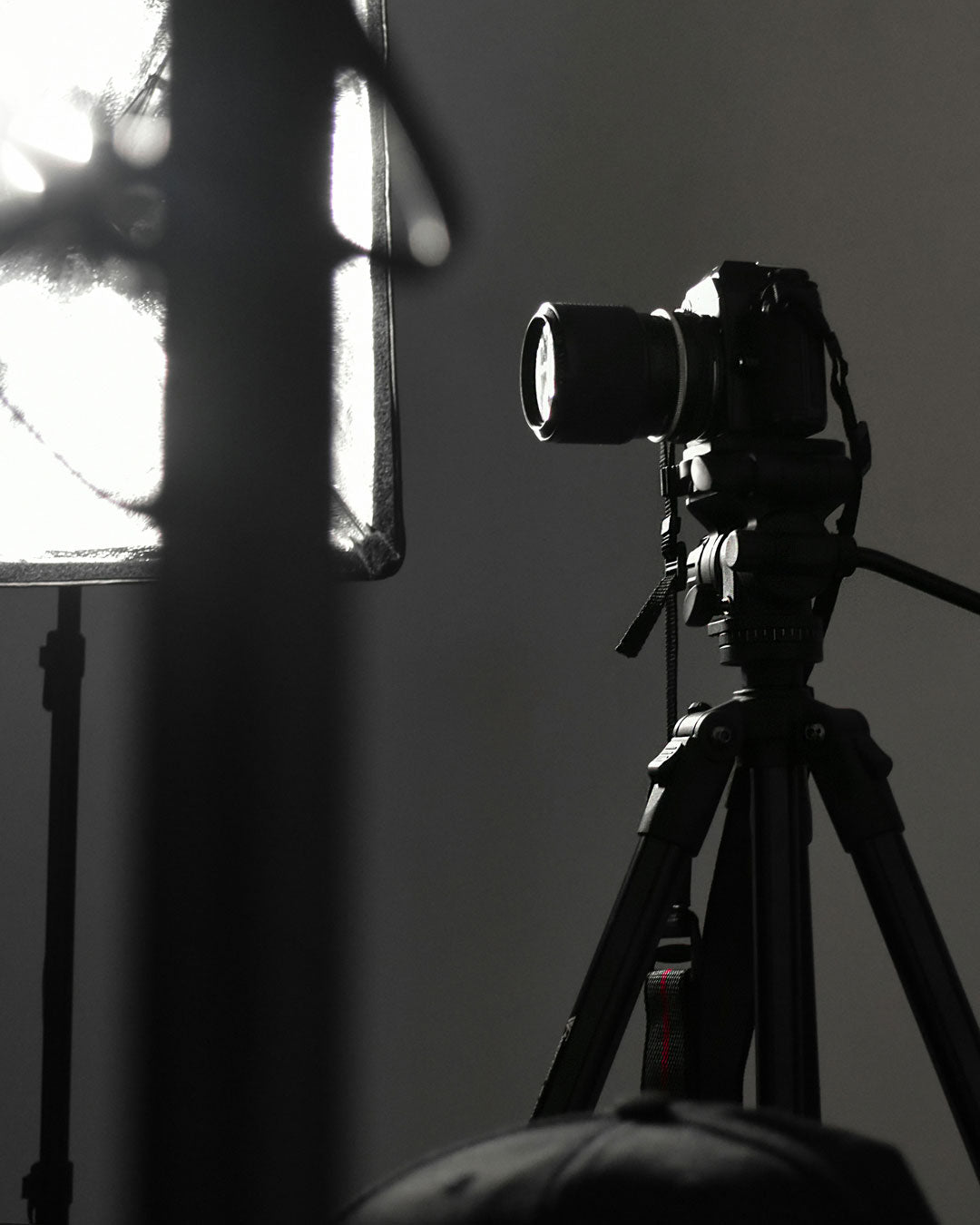 Studio photography setup with camera on tripod beside a softbox light, showing a behind-the-scenes professional eCommerce product photography scene in a dark studio.