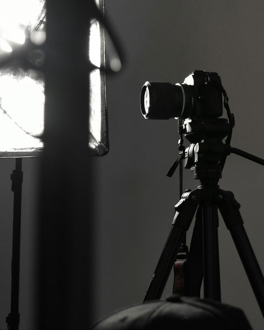 Studio photography setup with camera on tripod beside a softbox light, showing a behind-the-scenes professional eCommerce product photography scene in a dark studio.