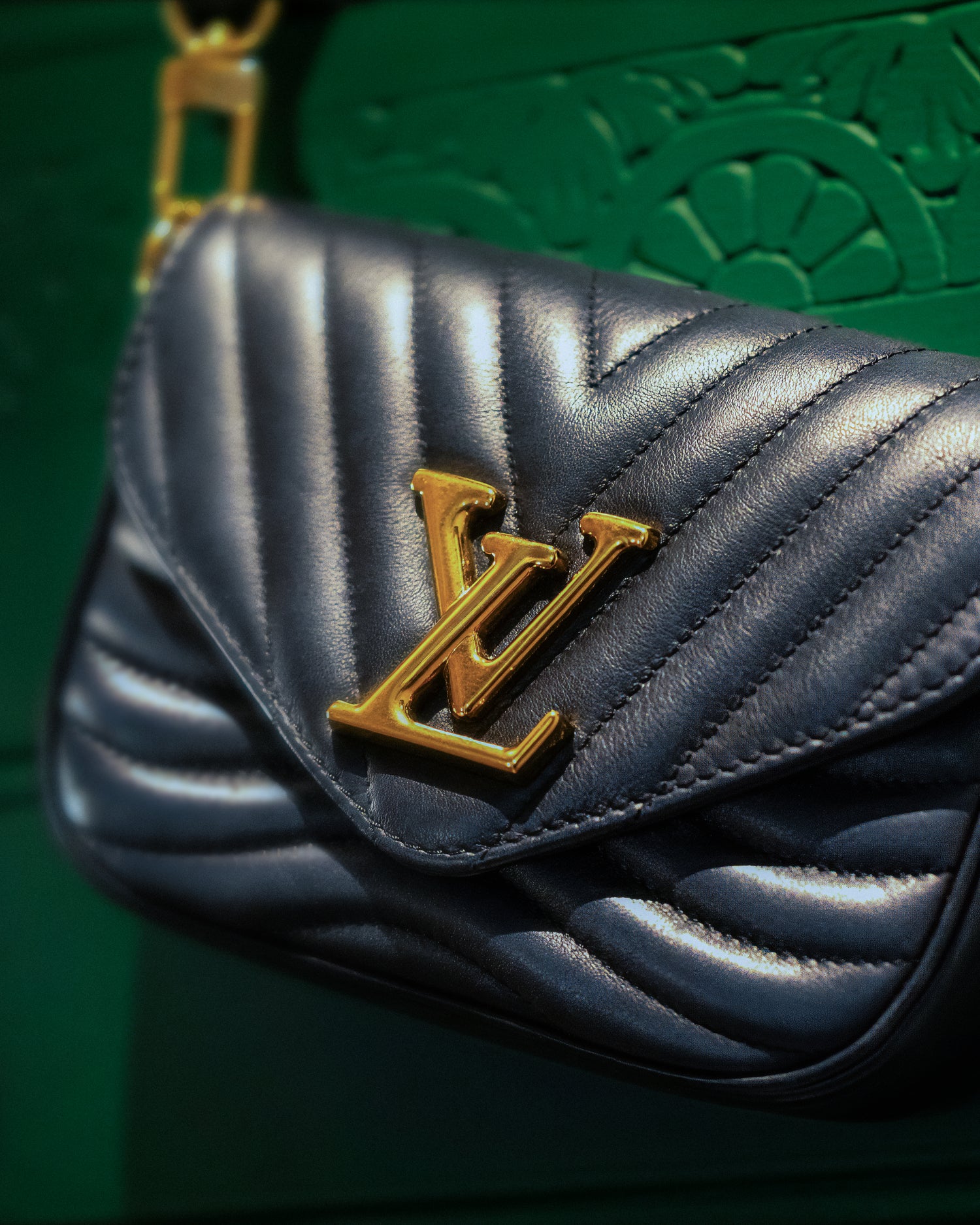 Luxury product photography of a black quilted Louis Vuitton handbag with gold logo detailing, captured in a dramatic close-up against a rich green textured background. Styled with warm highlights and shallow depth of field, the image showcases premium fashion accessories, editorial product photography and creative detail imagery by Badsatan in Harrogate, North Yorkshire.